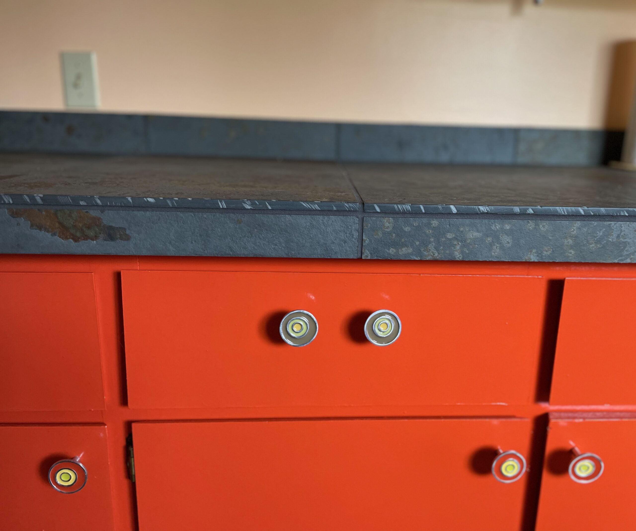 Grey tile counters with brown and orange tints. Unique and colorful pulls on cabinets - round swirl pattern in different colors.