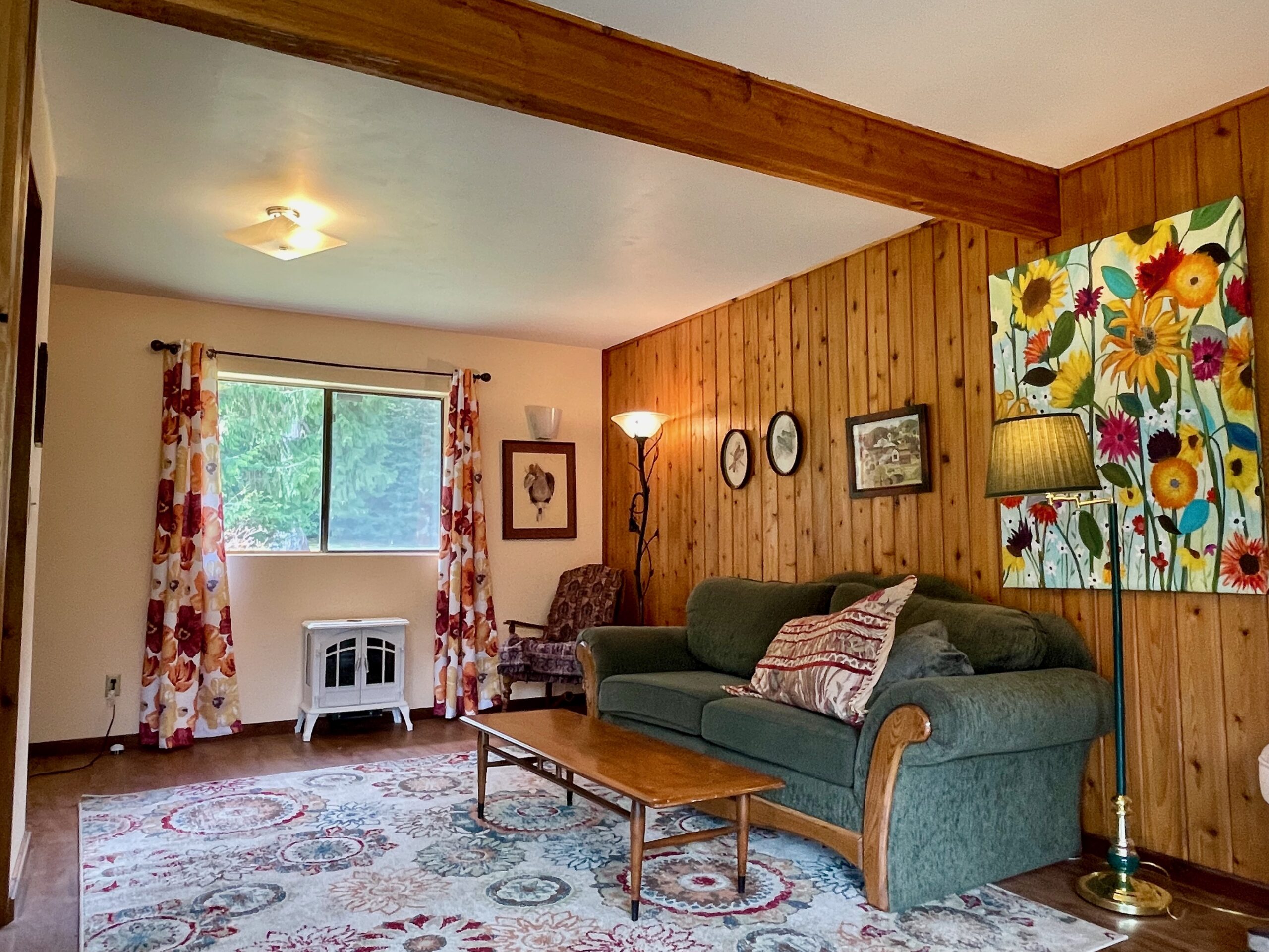 The south end of the living room which is painted a warm cream color and has a window looking out on the pines in the back yard.