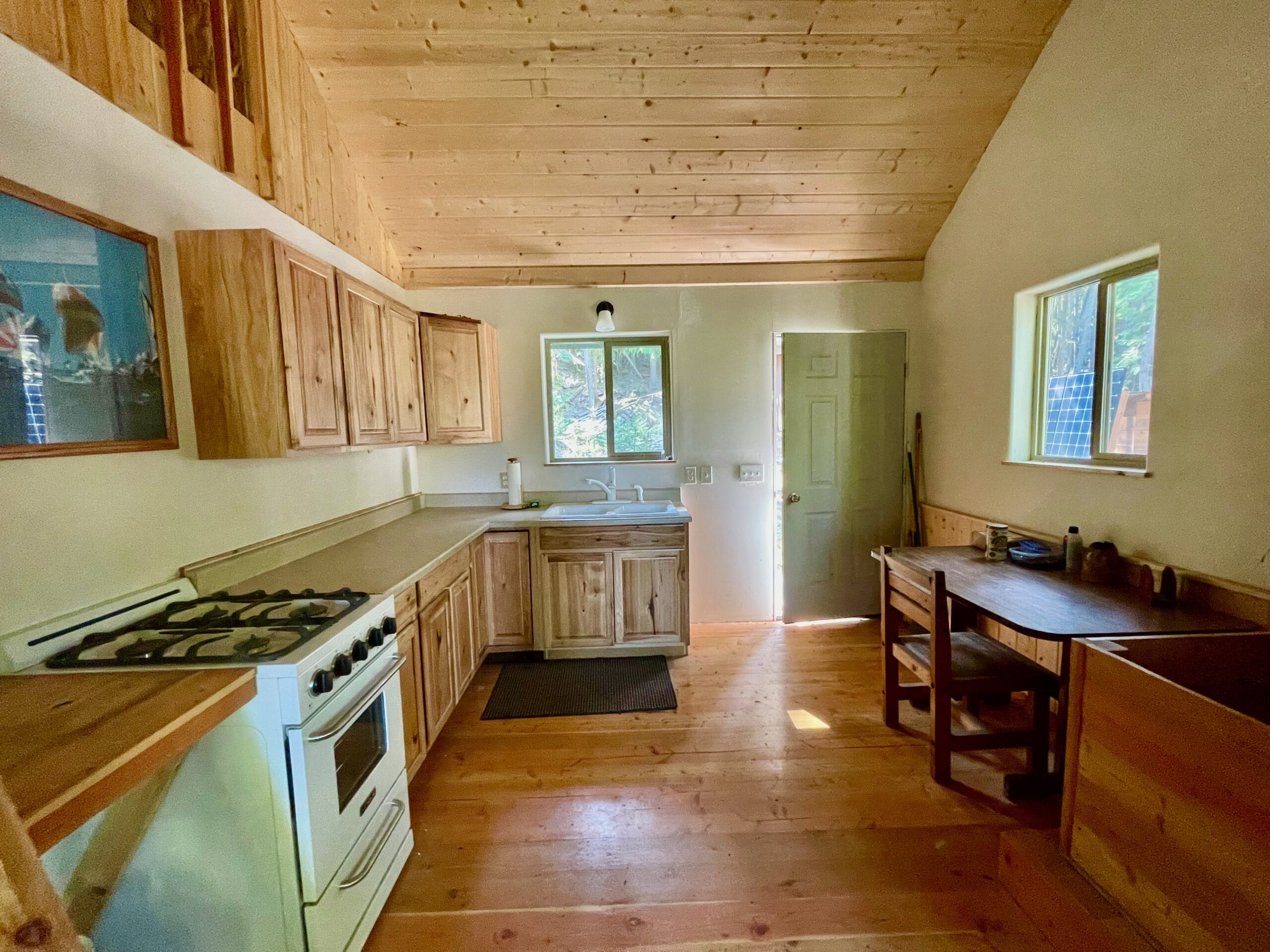 Looking from the living room to the front door with the stove and cabinets on the left, table on the right and door and sink in the background.