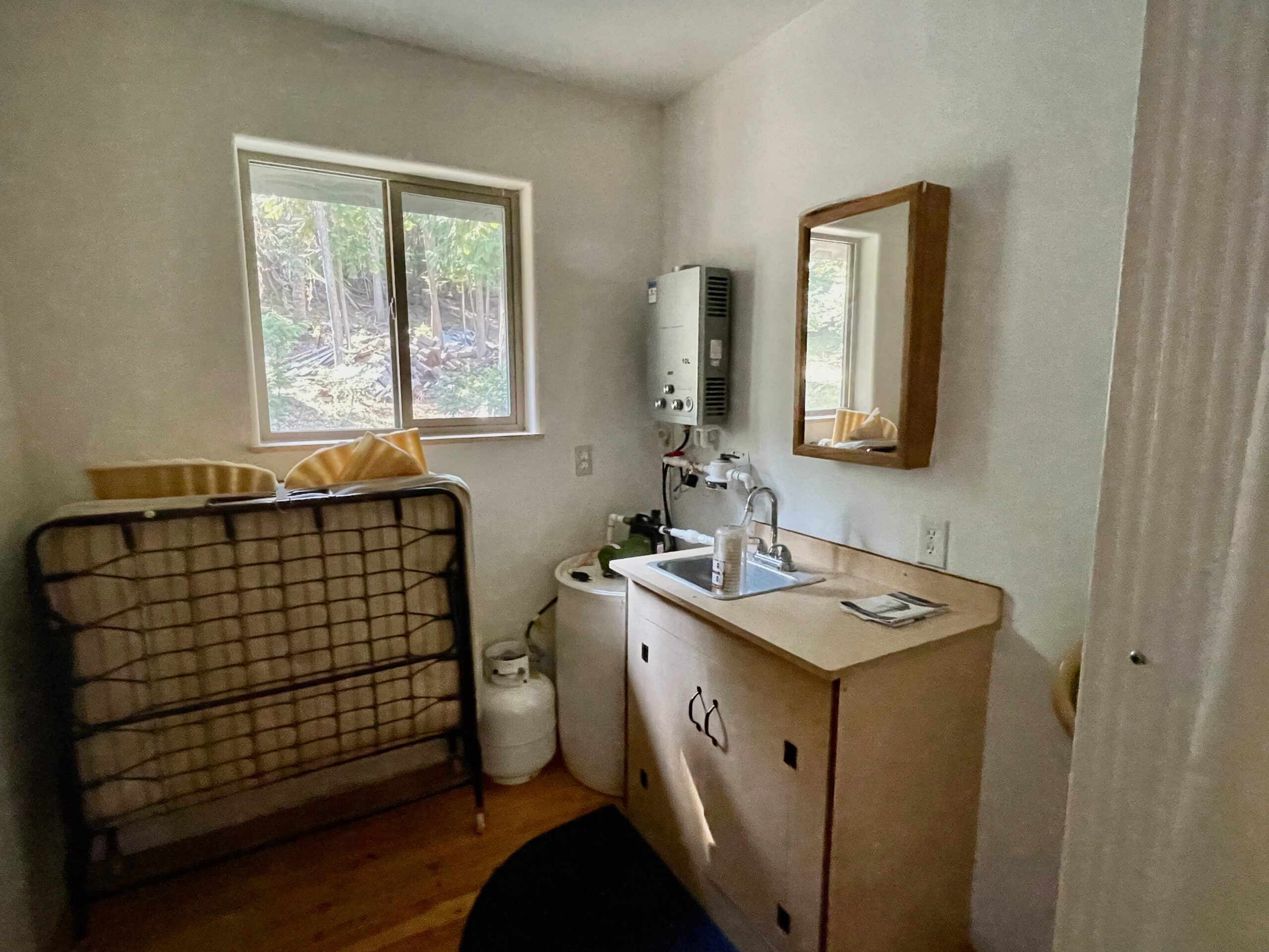 The bathroom sink, wall mirror, water  system and  with window looking out into the front yard.