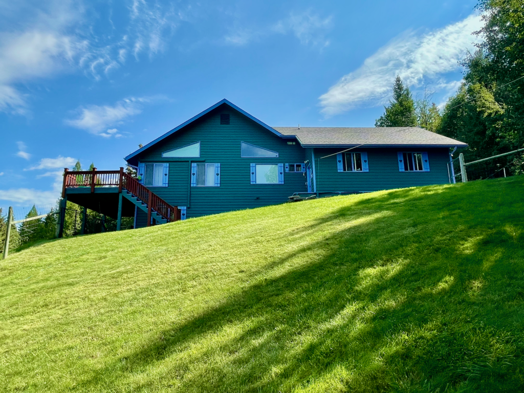 The west side of the house with stairs to the master-deck on the left, garage on the right, and the lawn in the foreground.