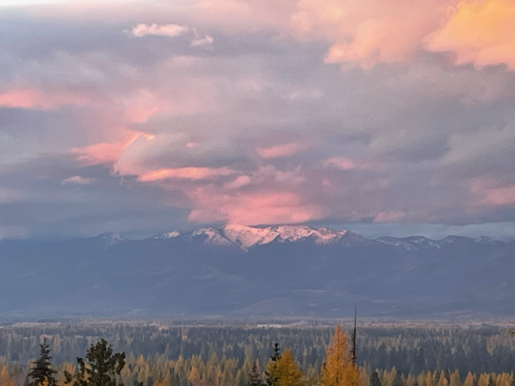 Amazing pink and white clouds over the snowy purple Swan Mountain Range Peaks.