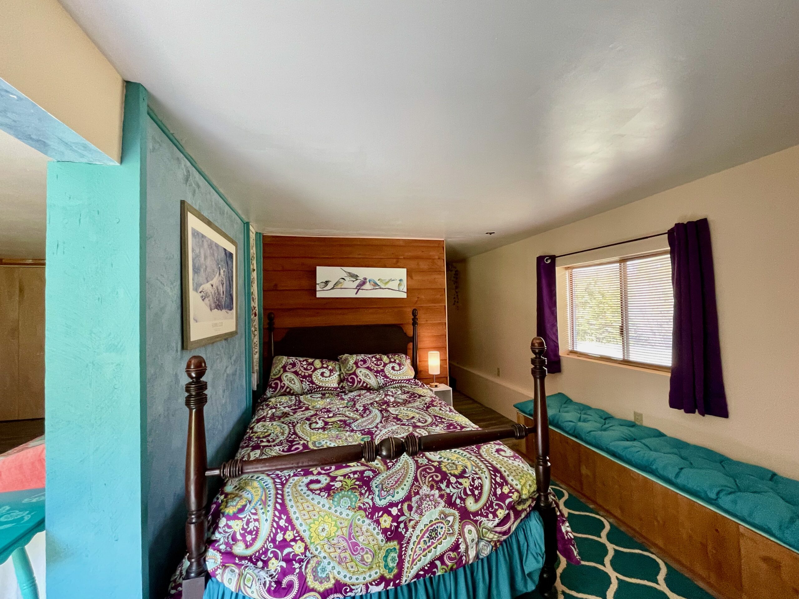 On the other side of the partial wall is another room which is being used as a bedroom. There is a bench for sitting under the window.